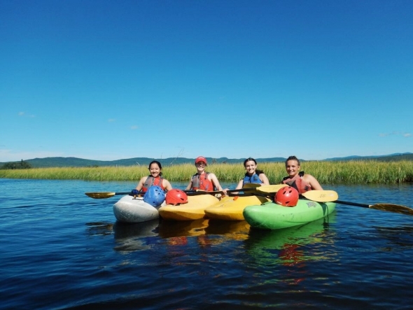 Abbi kayaking with 3 other friends on a large lake with mountains in the background