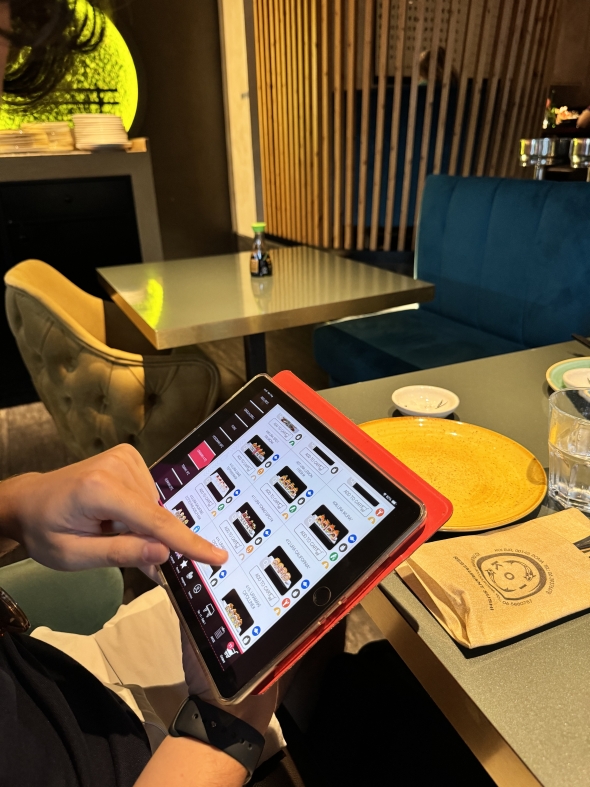  A person pointing at photos of sushi on an iPad while ordering at a restaurant.