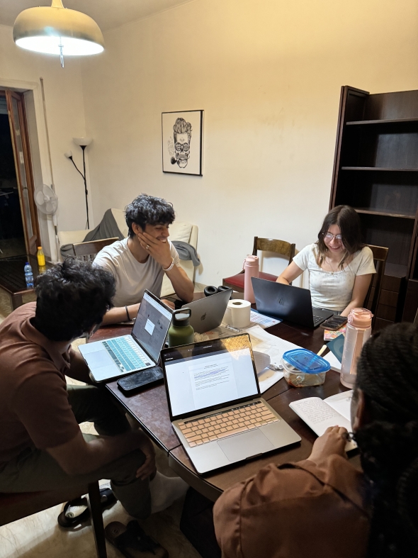 Four students sitting at a table with their laptops doing work.