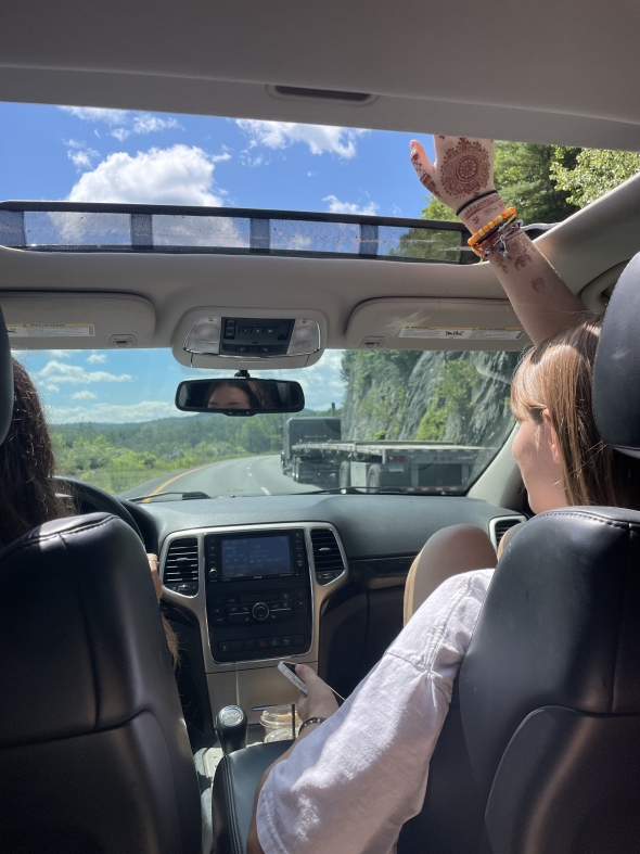 Drive through Vermont high-way showing a girl putting her hand through the sun-roof. Granite rocks and trees in the background