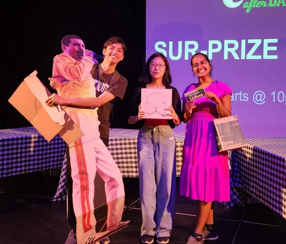 A photograph of 3 people each holding up a Bingo prize. Left: a male figure holding a life-size cardboard cutout of Freddie Mercury. Middle: a female figure holding up a box of Airpod Pro Max. Right: A female figure holding up an L.L. Bean gift card.