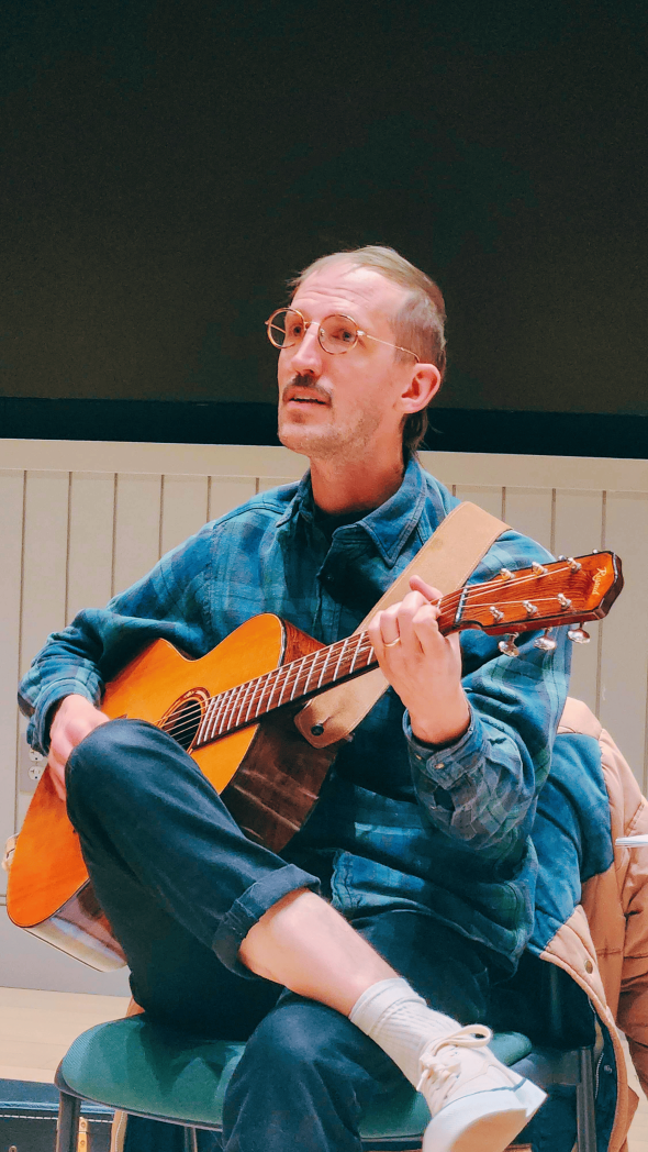 A man wearing denim singing while playing the guitar.