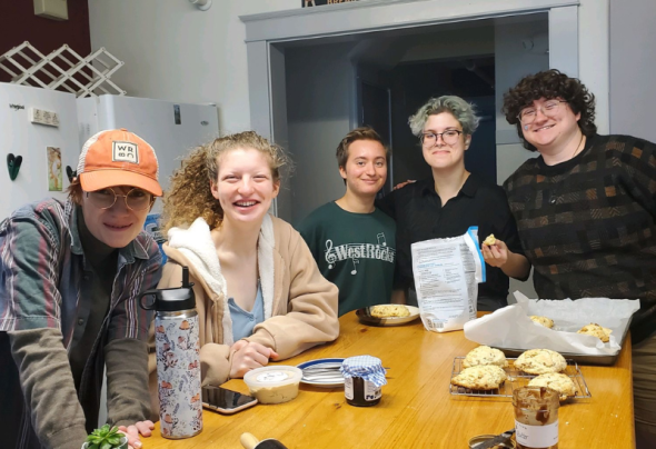 A photograph of 5 people gathered around a wooden table baking cookies