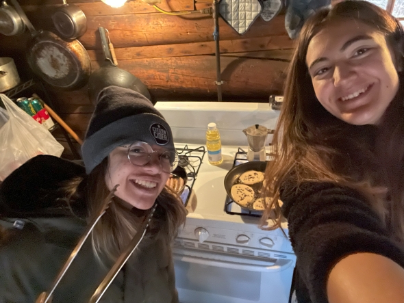 Scarlet and Kalina are taking a selfie by the pans of sausages and pancakes