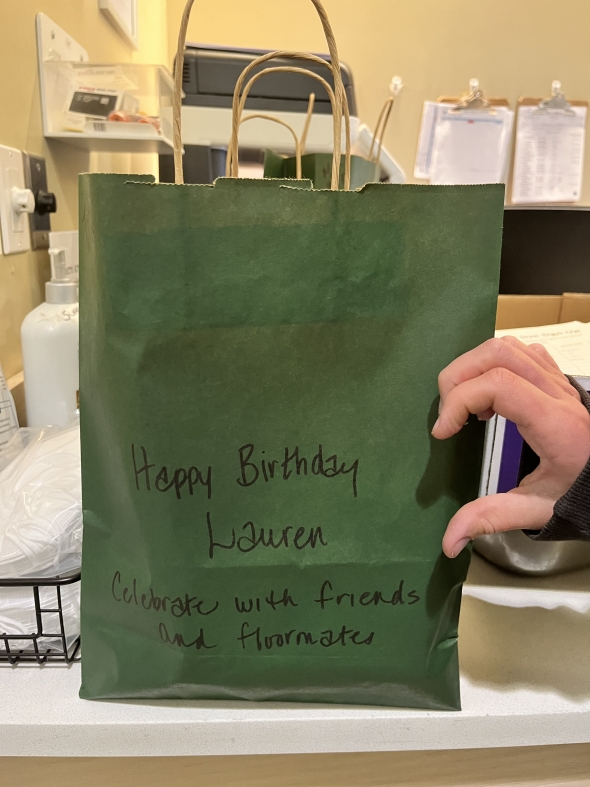 A green bag that says "Happy Birthday Lauren! Celebrate with friends and floormates" sitting on a counter inside the dining hall