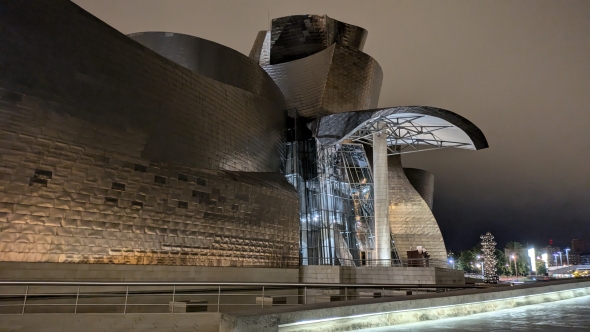 This a picture of the guggenheim museum at night from a view close to the river meaning further from the city center.