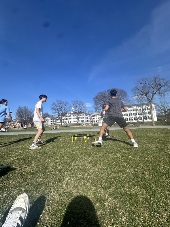 Four people are playing spike ball with the net in the middle of their circle; they are on the Dartmouth Green.