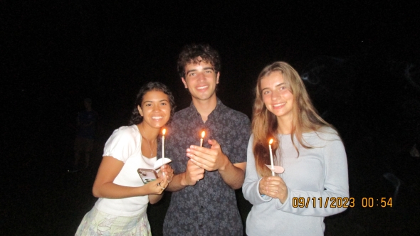 Gabriela standing with two friends at the Twilight Ceremony holding lit candles. 