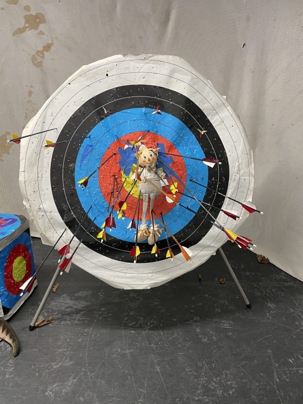 A picture of a target and a doll taped to it, pierced with many arrows