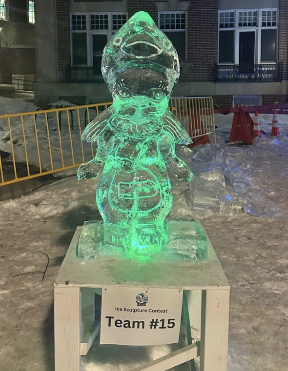 An ice sculpture of an angel with detail is perched on top of a small table and a label for the ice sculpture contest.