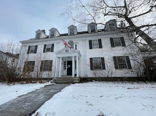  a picture of the Greek house Alpha Theta, seen from the street: a white house with a flag 