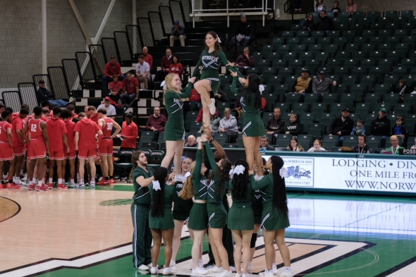 The Dartmouth cheer team doing a pyramid stunt in the middle of the basketball court during halftime at a game.
