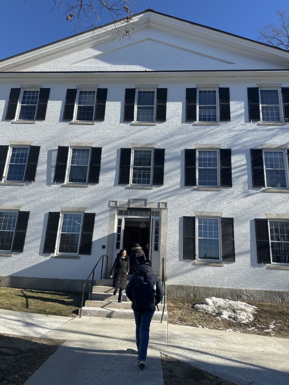 White brick building with students walking in and out of the door.