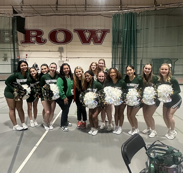 A cheer team smiles brightly at the camera, donned in green uniforms and green and white pom poms.