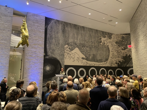 A wide atrium filled with a crowd gather around artist Cara Romero as she gives her opening remarks for her exhibit at the Hood Museum