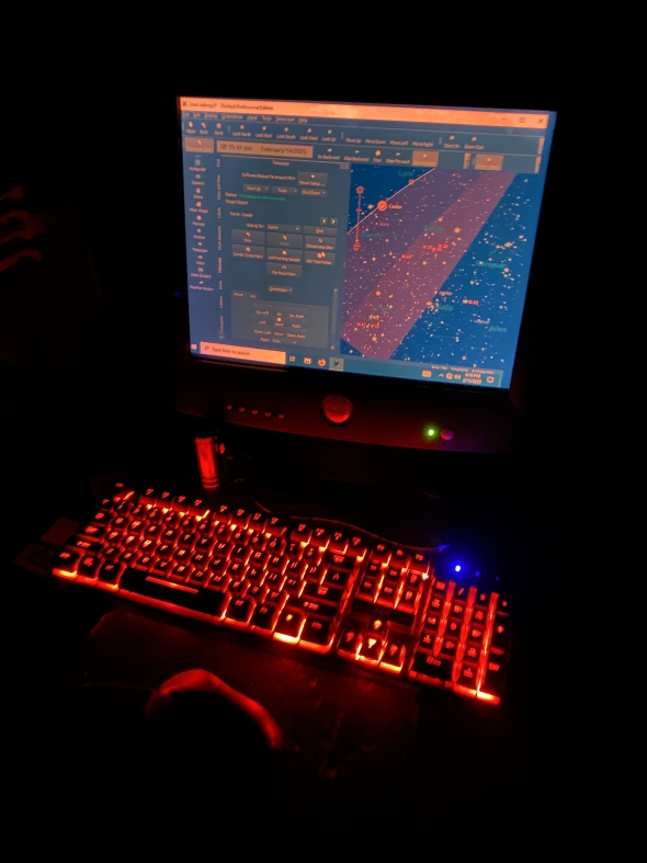 A computer monitor displays astronomical charts in front of a glowing red keyboard in the dark. 