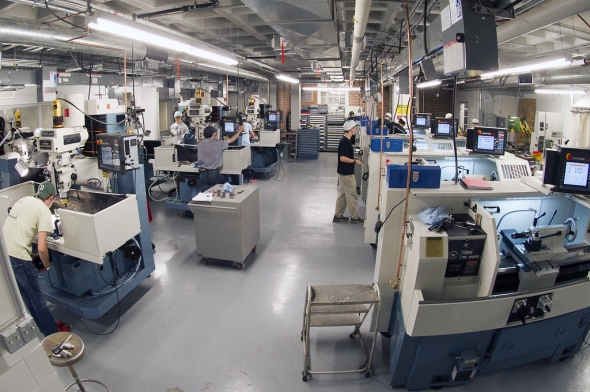 A landscape shot of the machine shop's CNC machines lit by fluorescent lighting in an industrial space.