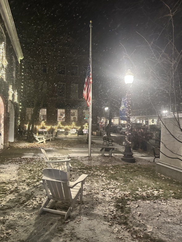 Snow falling on grass with an American flag pole in the middle.