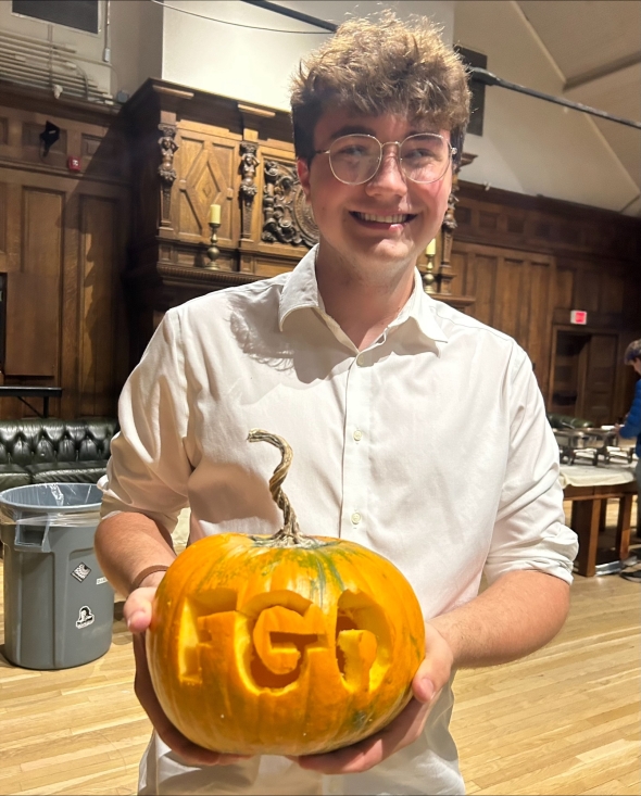 A carved pumpkin with the letters 'FGO' proudly displayed, held by a student at the First-Year Community Dinner.