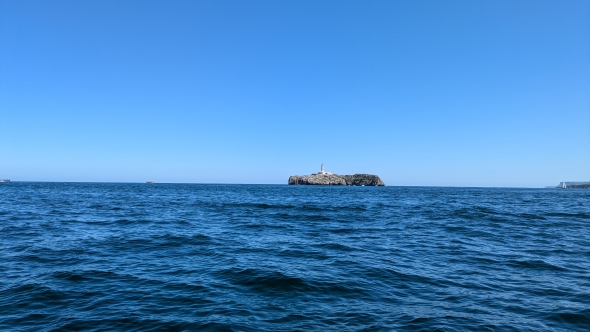 A photo mostly composed of dark blue ocean water. An island with a lighthouse is also prominent.