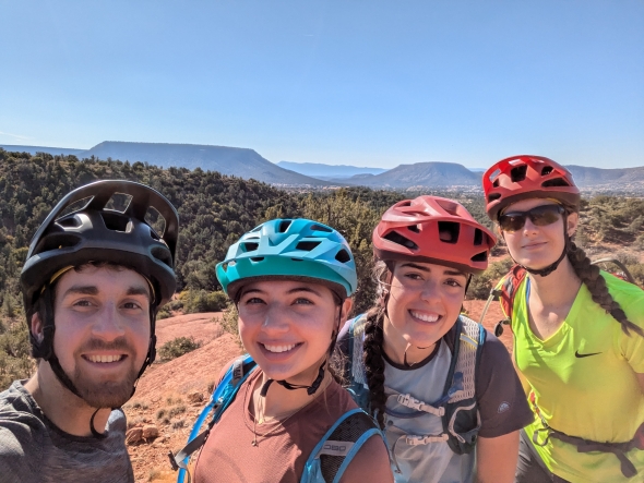 This is a photo of the upper torso of four mountain bikers in Arizona. This picture was taken on the top of a mountain plateau after a long climb and everyone is wearing their helmets.