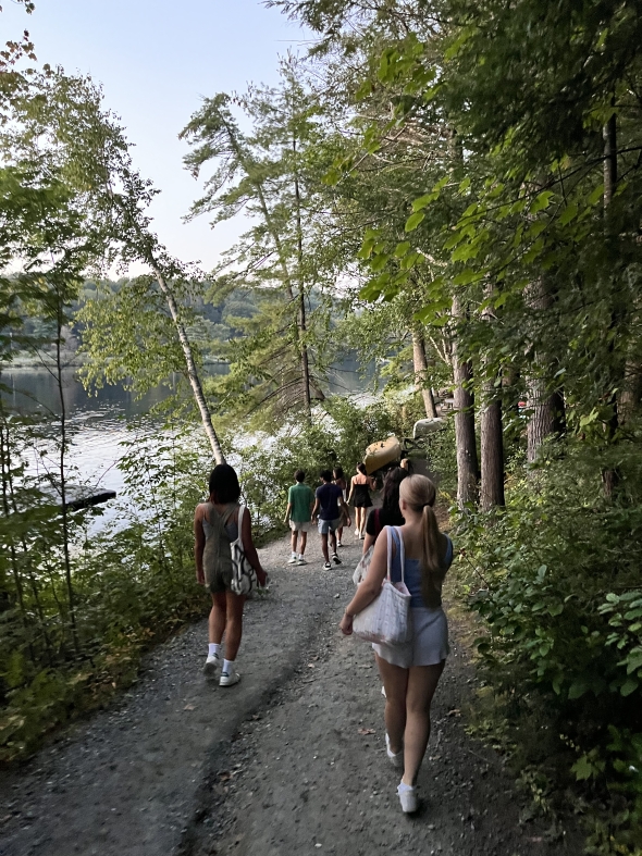 A photo, taken at dusk, of a group of students walking down the dirt path to the Connecticut River. 