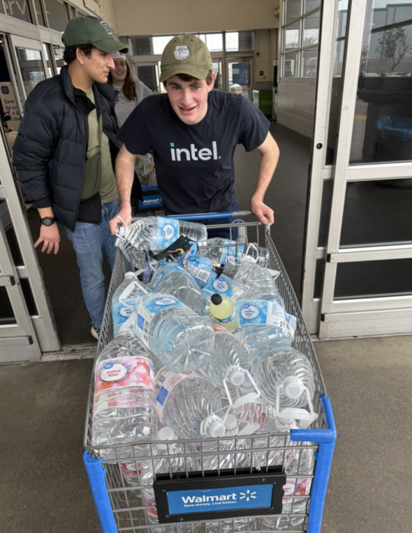 A man pushing a filled shopping cart of monstrous water gallons outside of a mart.