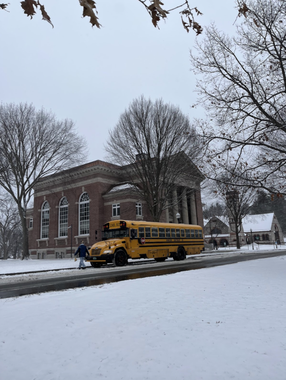a yellow school bus waits on the side of the road. Snow covers the ground.