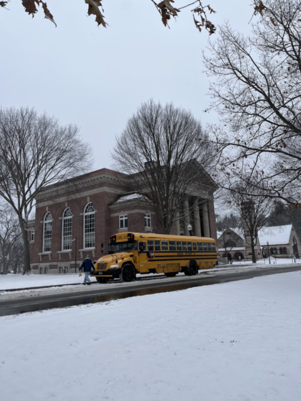 a yellow school bus waits on the side of the road. Snow covers the ground.