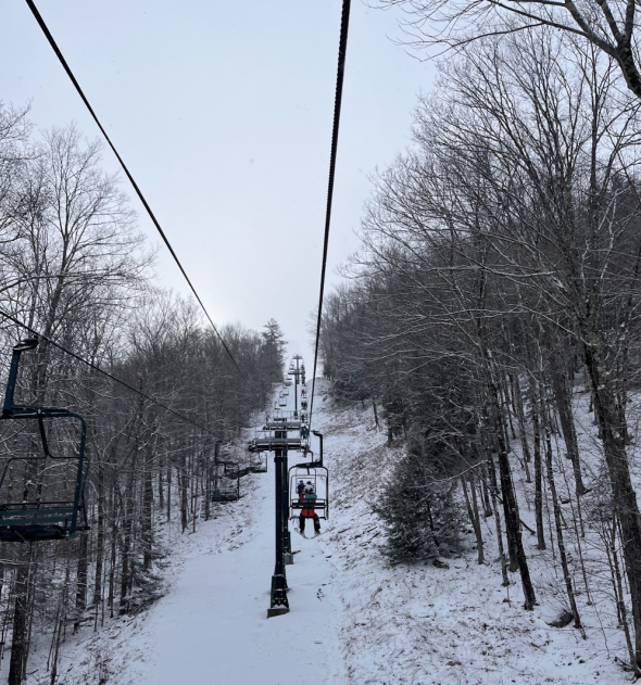 a picture of the ski lift, taken from one of the ski lift chairs. There are trees on either side.