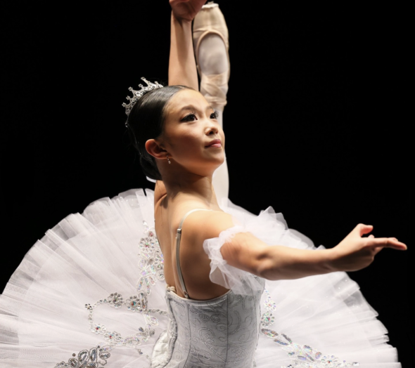 An image of me, Crystal, in the middle of a dance performance. I am wearing a white tutu and pointe shoes. My left leg is up in an extension.