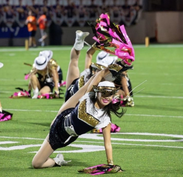 An image of me, Crystal, on a football field in the middle of a performance. My right leg is in an extension and I am holding a stream.