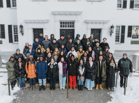 An image of students gathered on the steps outside a building and smiling at the camera