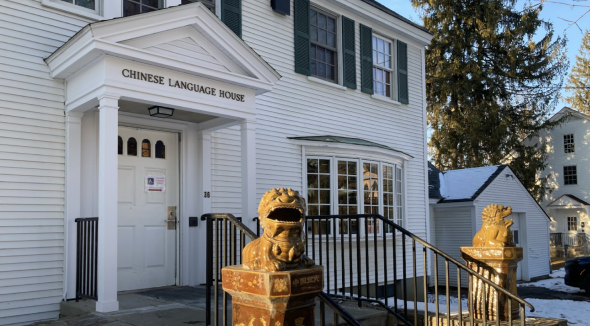 The front door of the Chinese Language House. The Chinese Language House is a white house with horizontal paneling. Towards the foreground are two brown Chinese lion statues on both sides of the staircase.