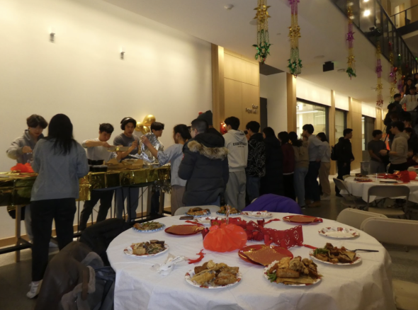 A view of DCSA volunteers serving food to attendees. In the foreground is a round table covered in a white tablecloth. The table has various red decorations and plates of food on top. 