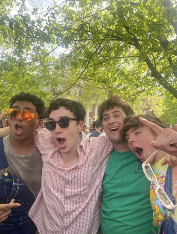 An image of four students outside at a celebration. They appear to be singing or shouting and the background is light.