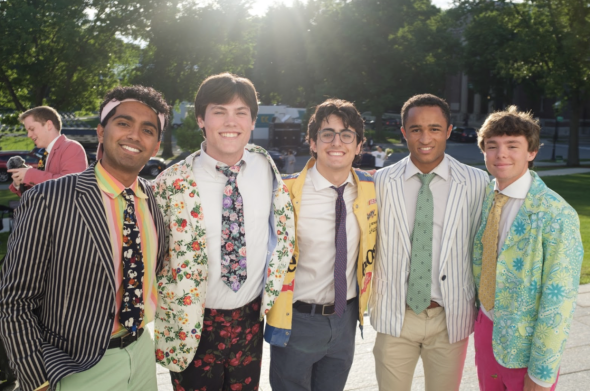 A group of five students outside. They are wearing colorful suits and there are trees in the background.