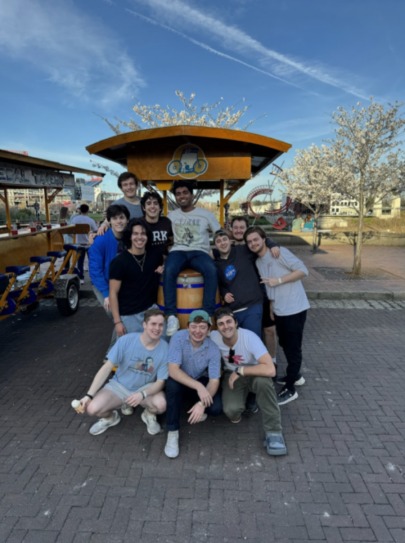 A group of students outside posing with a cart. The background is light and the setting seems to be a public park.
