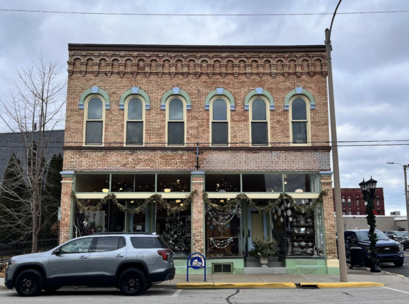 A brick store building in Bay City with a parked car in front of it. The store's windows are decorated with Christmas lights and garland.