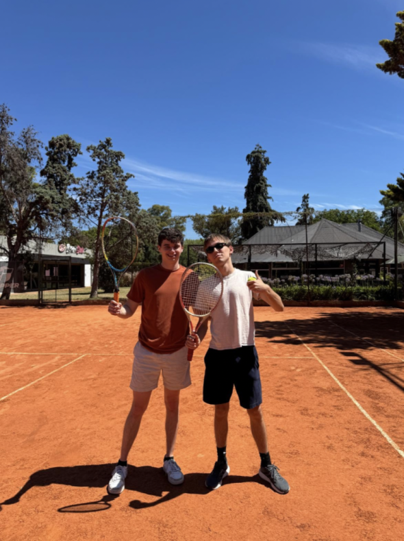 Two Dartmouth students posing with tennis racquets on a clay court.
