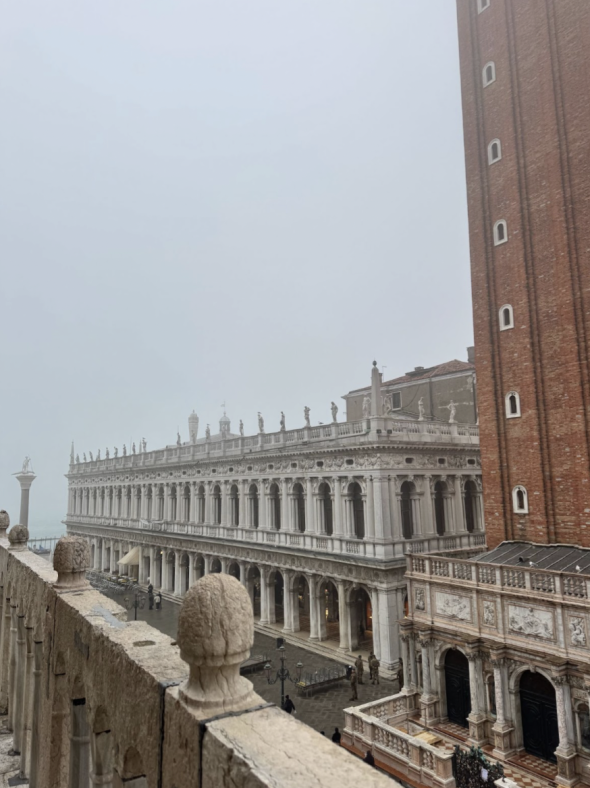 Multiple Medieval and Renaissance buildings, as seen from a balcony. It is a foggy day, so the Venetian Lagoon in the background is hardly visible.