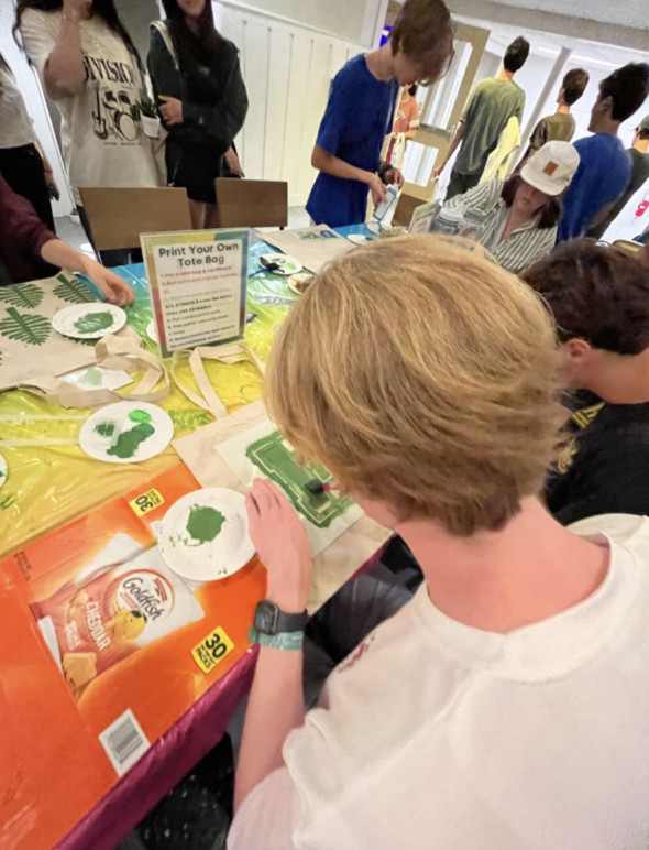 Students gathered around a table painting tote bags with green paint at Collis.