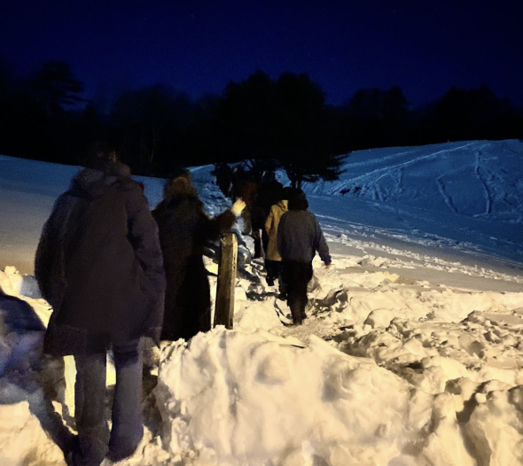 A group of students walking in Pine Park at night. There is a lot of snow on the ground.
