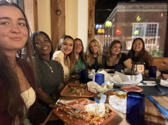 A group of students sitting in a restaurant booth and smiling at the camera.