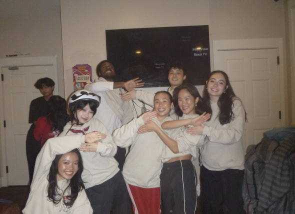 A group of students posing in a group formation. They are wearing beige hoodies and are in a fraternity room.
