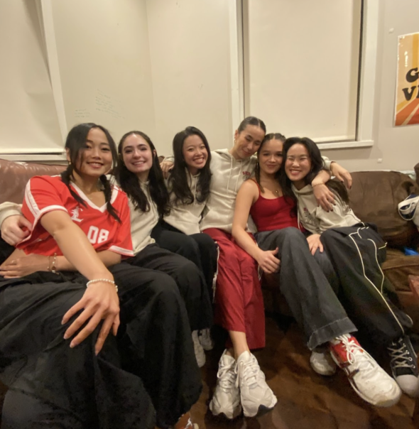 A group of students sitting on a couch and smiling. The students are group hugging.