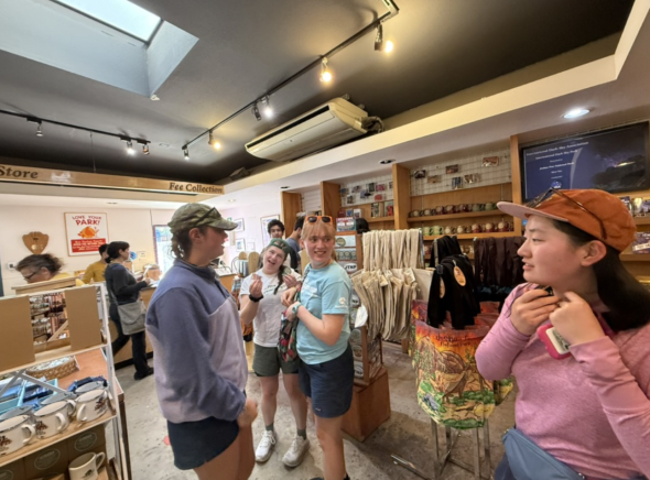 A bunch of students in the aisles of a merchandise shop trying out scarfs and tote bags.