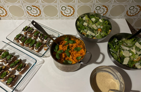 Eggplant bruschetta, spicy vodka pasta, salad, and Caesar salad dressing arranged in containers on the counter before dinner.
