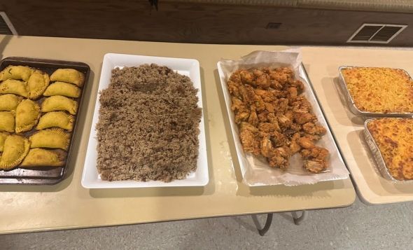 Four trays of food featuring patties, rice and peas, macaroni, and fried chicken presented on a table.