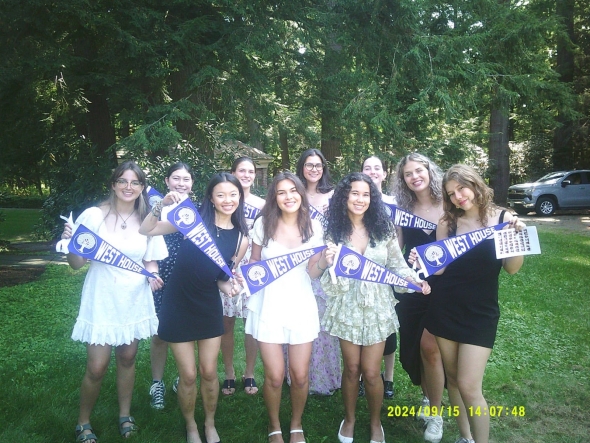 An image of me, Crystal, and all of my dorm floor friends. We are all holding purple flags that say "West House" on them. The background is in a wooded area and we are all standing on grass.